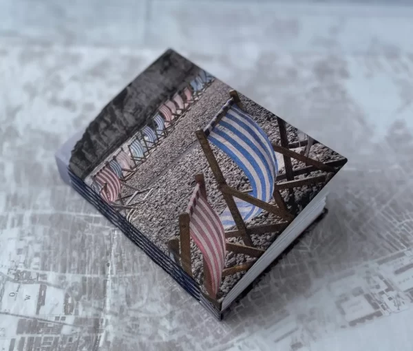 Cover of handmade book showing photo of striped blue and red deckchairs on pebble beach